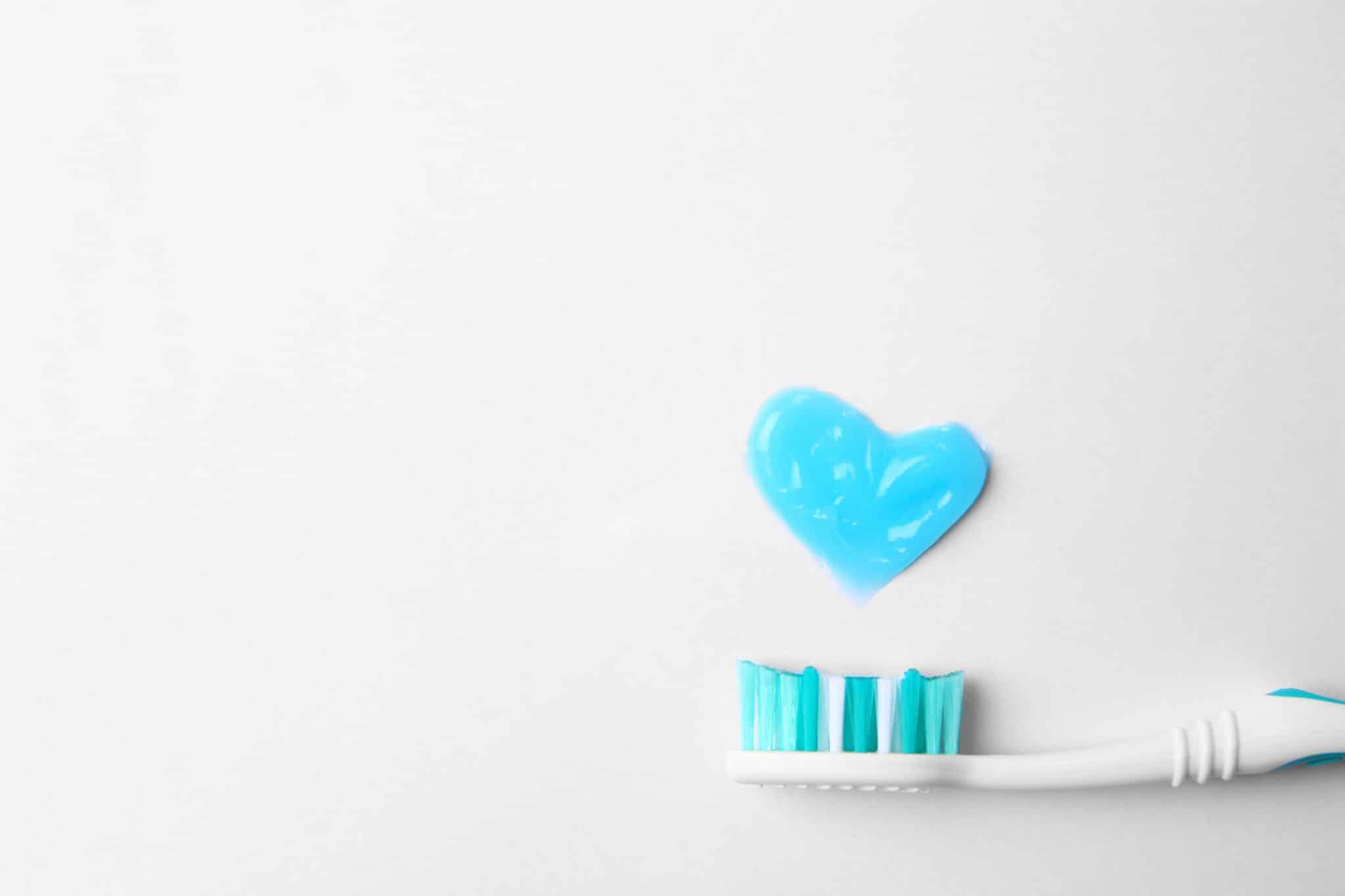 Herz aus Zahnpaste, darunter Ausschnitt einer Zahnbürste.