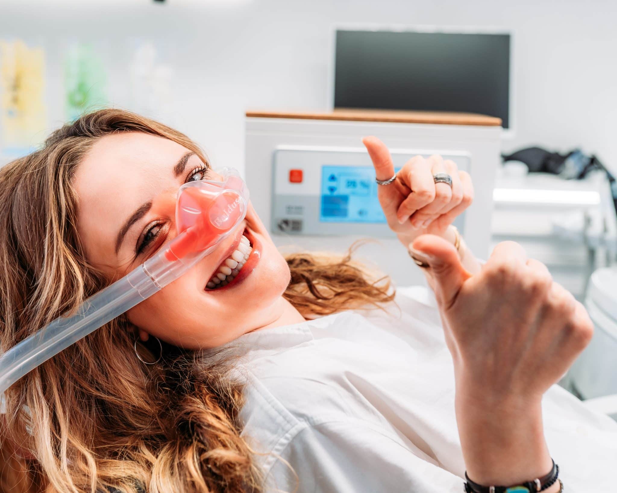 Frau mit Anästhesie-Maske im Zahnarztstuhl. Sie hält beide Daumen nach oben.