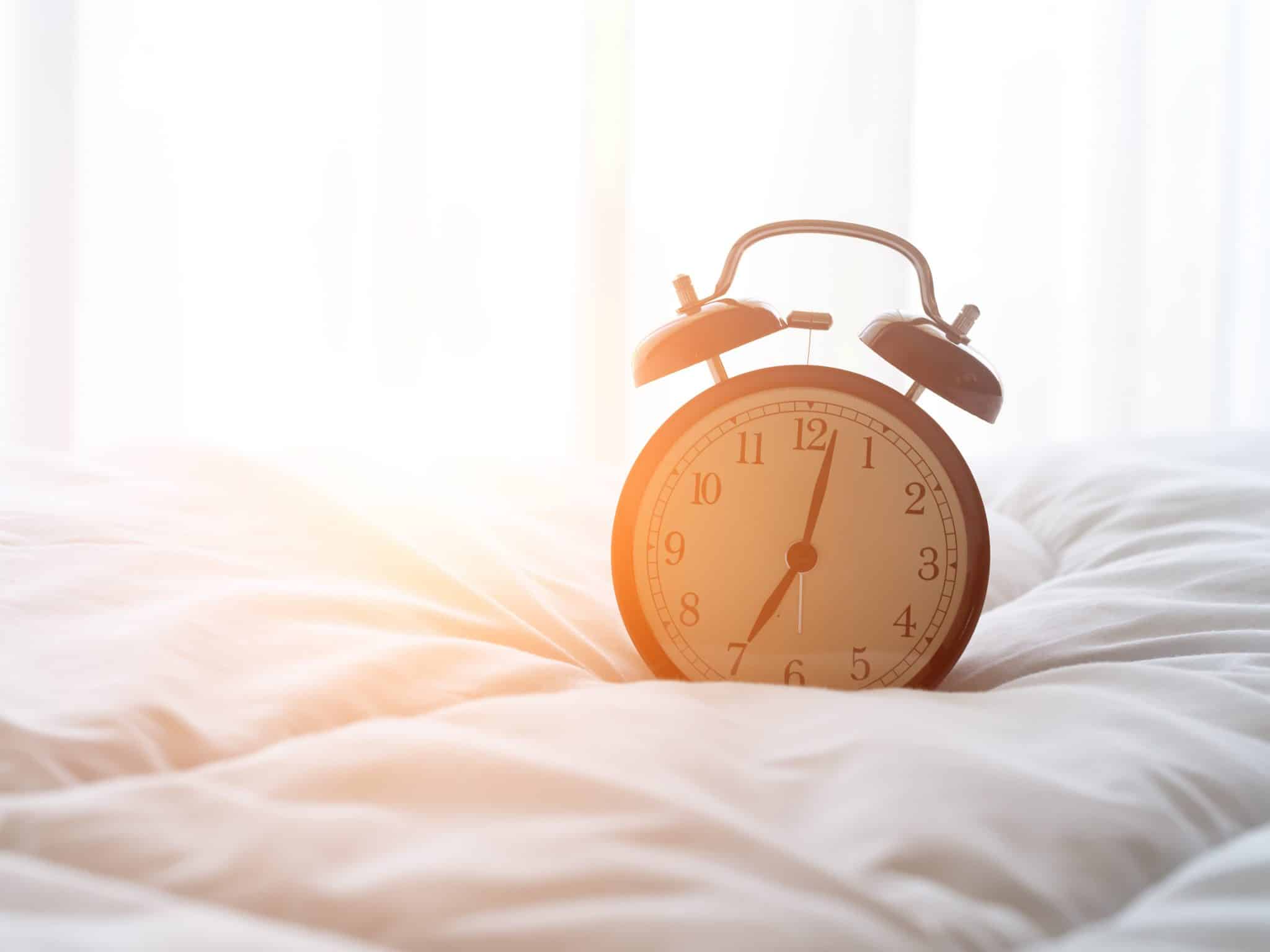 Ein Wecker steht auf einer Bettdecke in der Morgensonne.