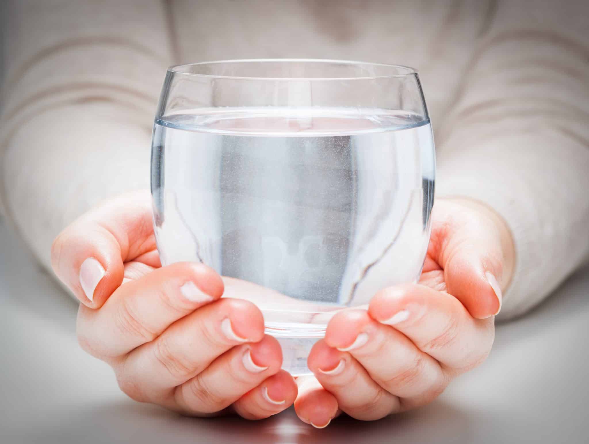 Zwei Hände, die eine große Glasschale mit Wasser halten