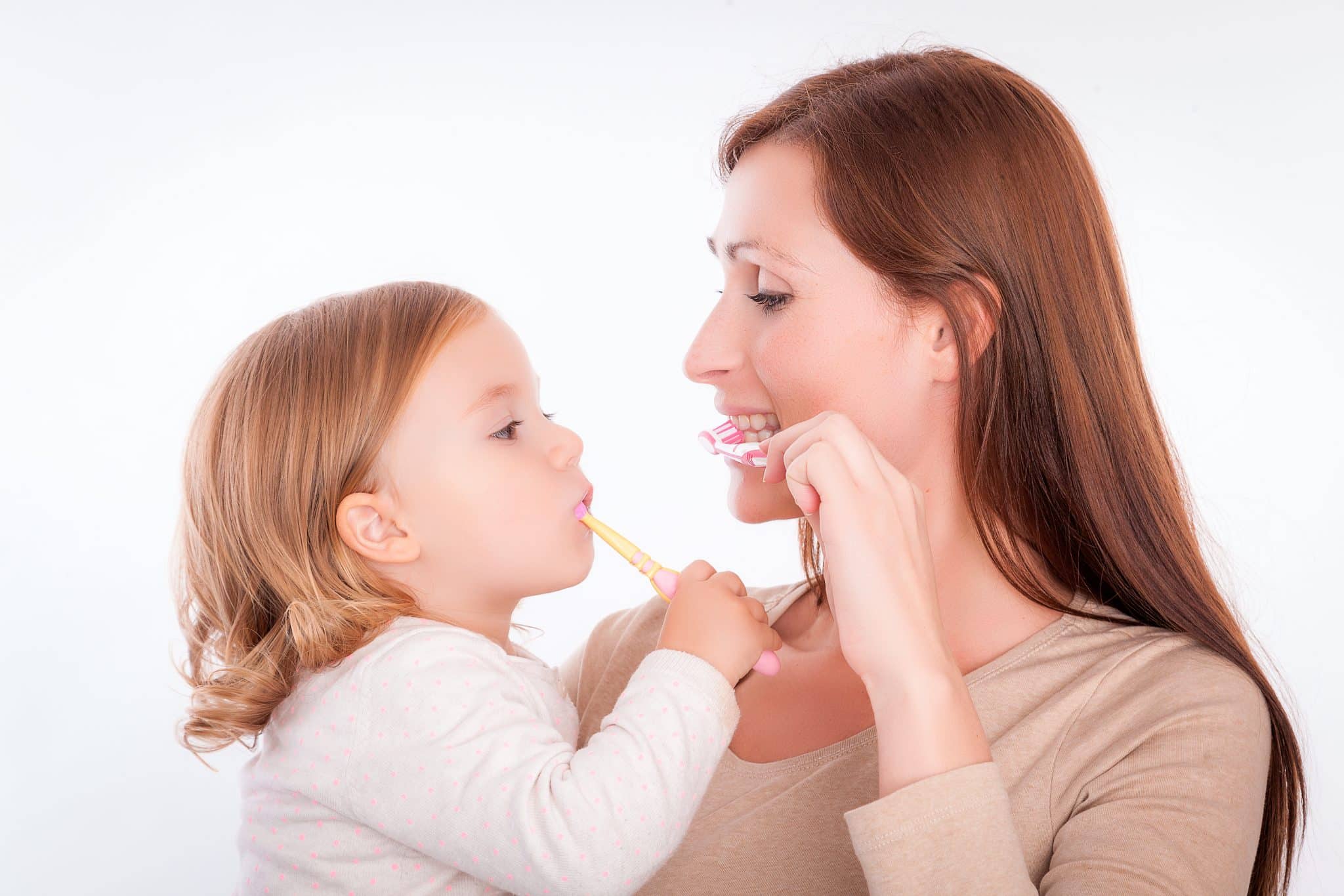 Frau mit Kleinkind auf dem Arm, beide halten eine Zahnbürste in der Hand und putzen sich die Zähne
