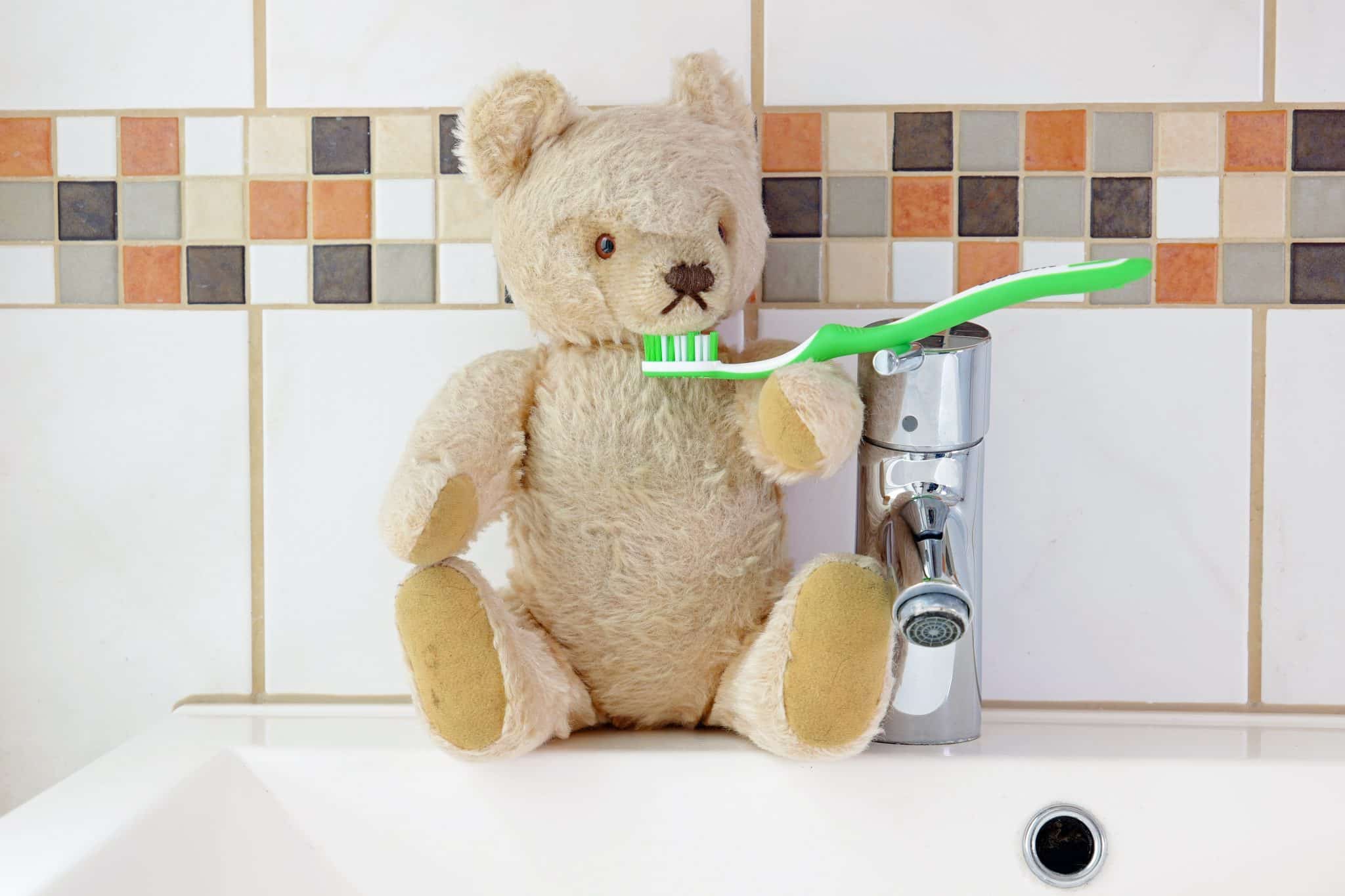 Detailaufnahme eines Waschbeckens, auf dem ein Teddybär sitzt, der eine Zahnbürste auf dem Arm hat