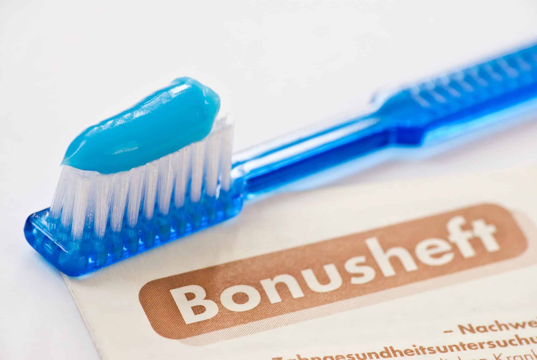 Zahnbürste mit blauer Zahnpasta, darunter ein Bonusheft