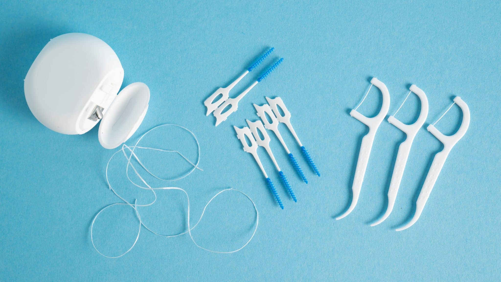 Zahnseide, Dental Picks und Zahnseidehalter auf hellblauem Untergrund