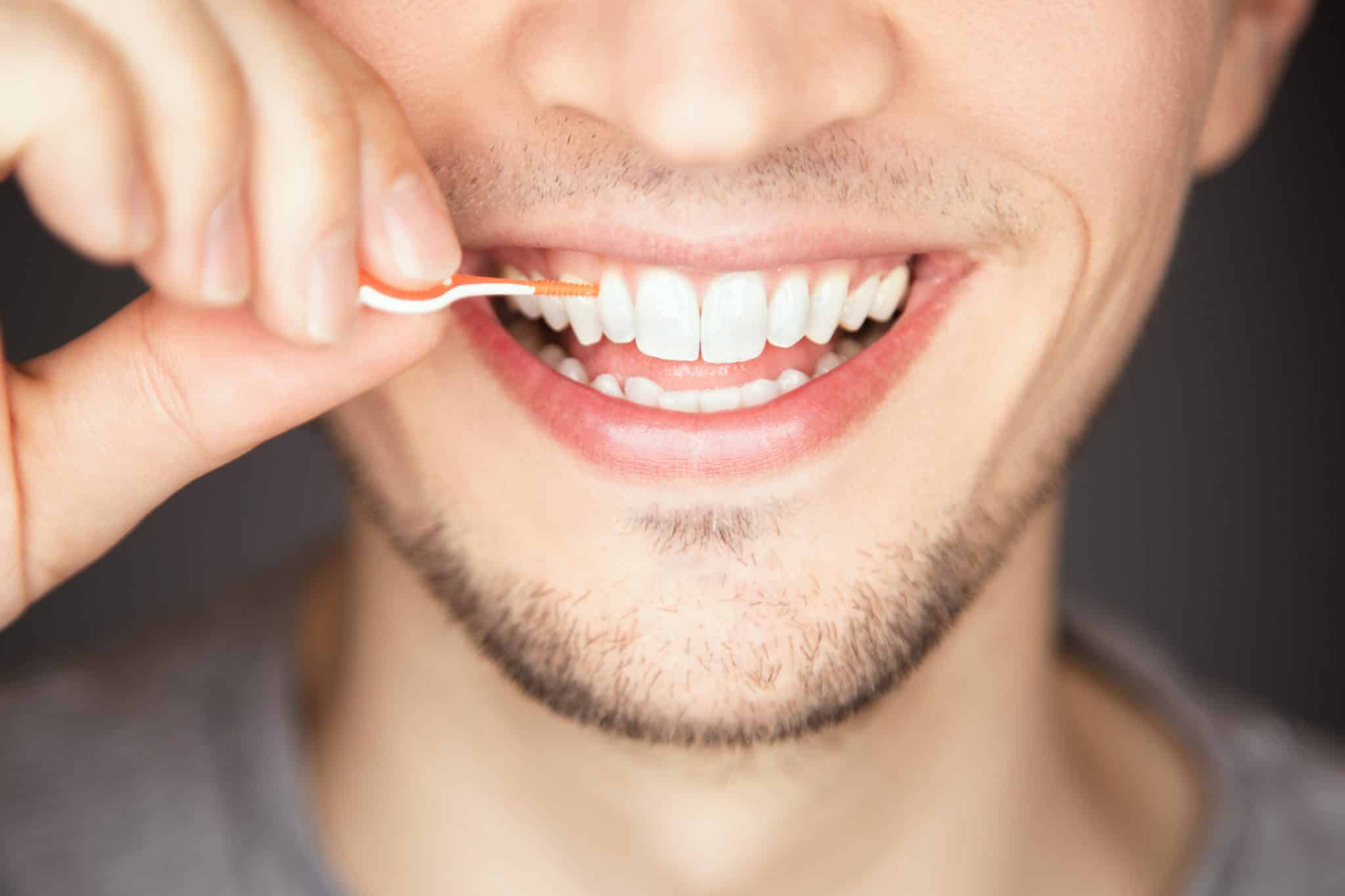 Strahlender Mann mit 3-Tage-Bart reinigt die Zahnzwischenräume mit einem Dental Pick