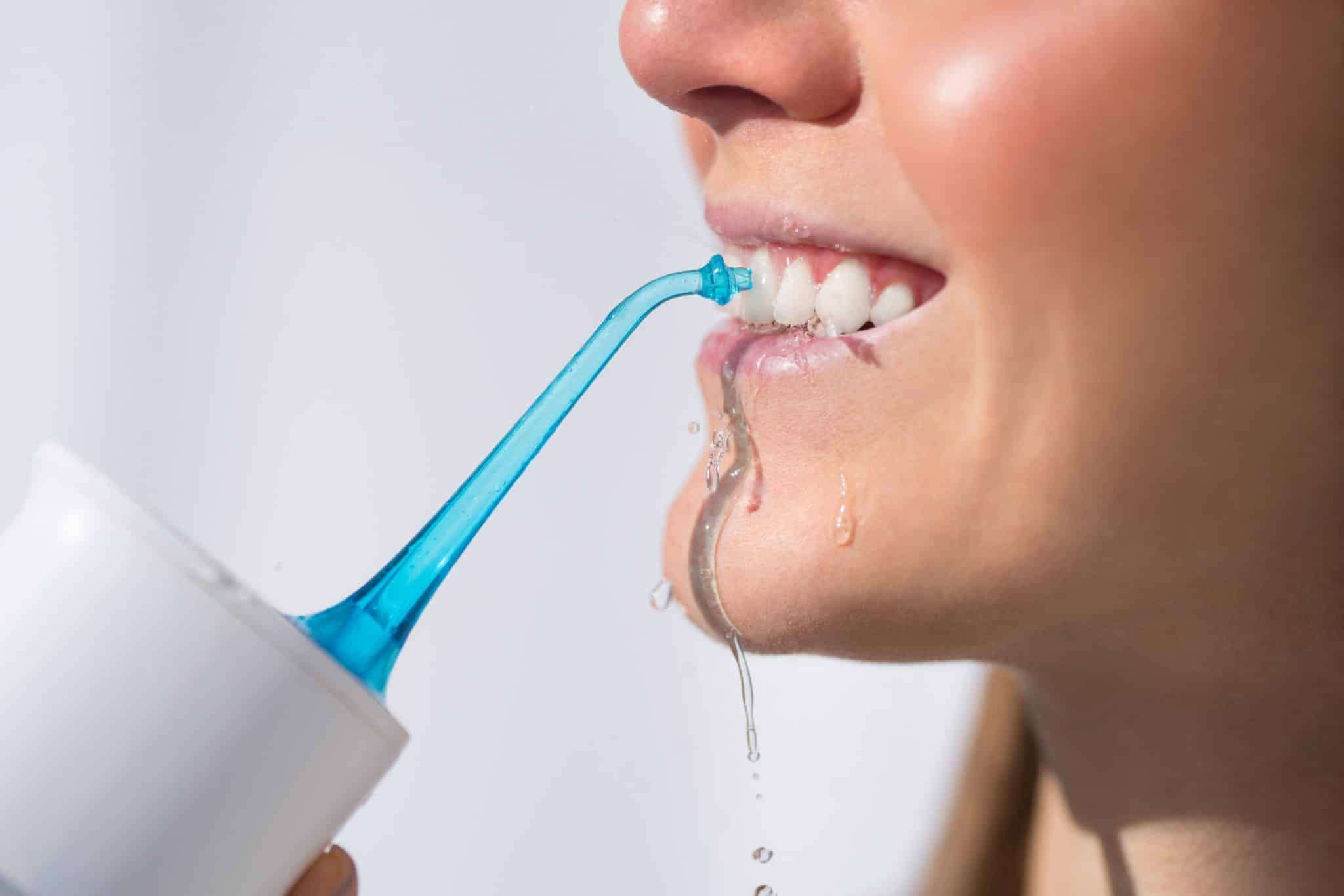 Lächelnde Person reinigt ihre Zahnzwischenräume mit einer Munddusche
