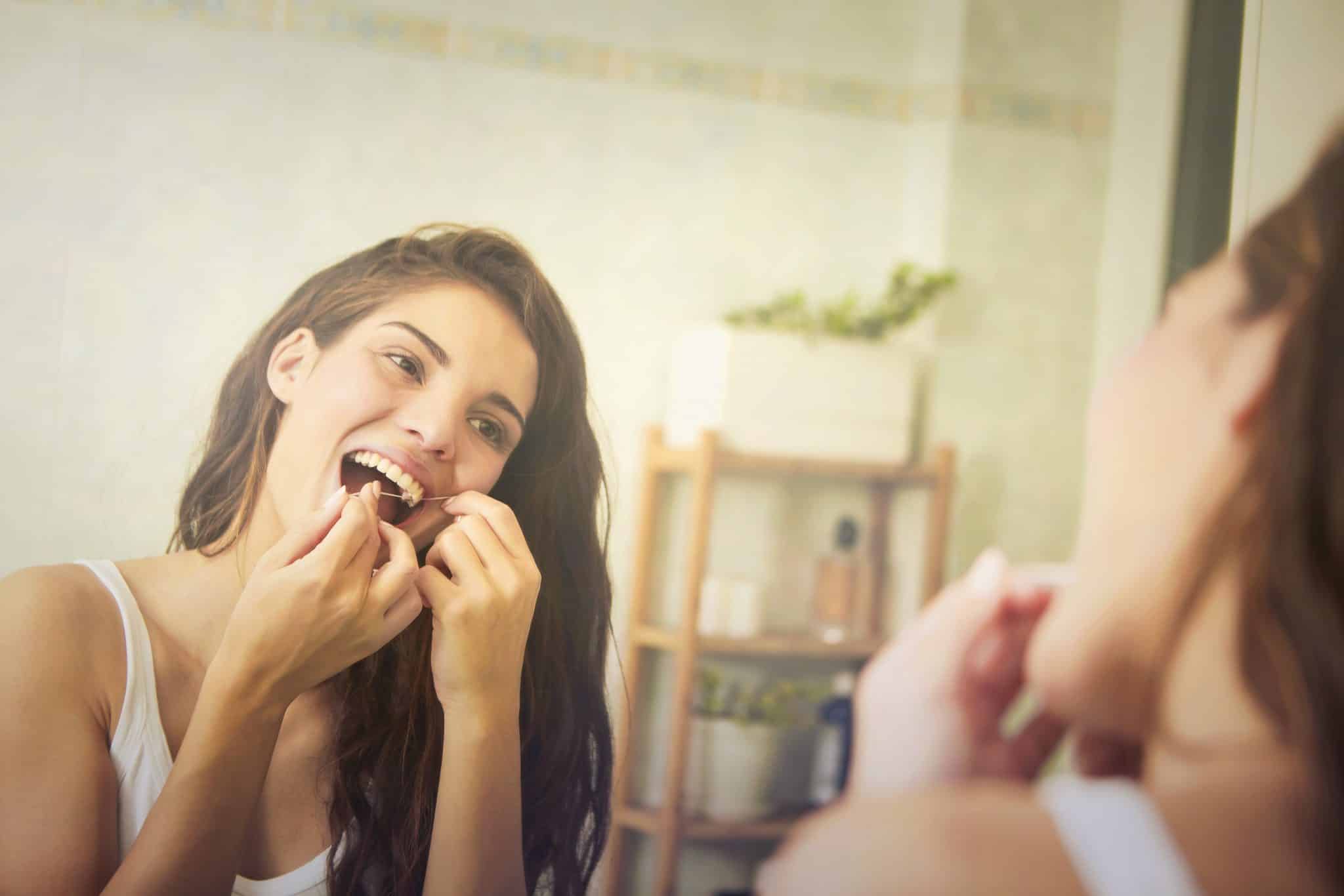 Frau vor dem Spiegel reinigt die Zahnzwischenräume mit Zahnseide