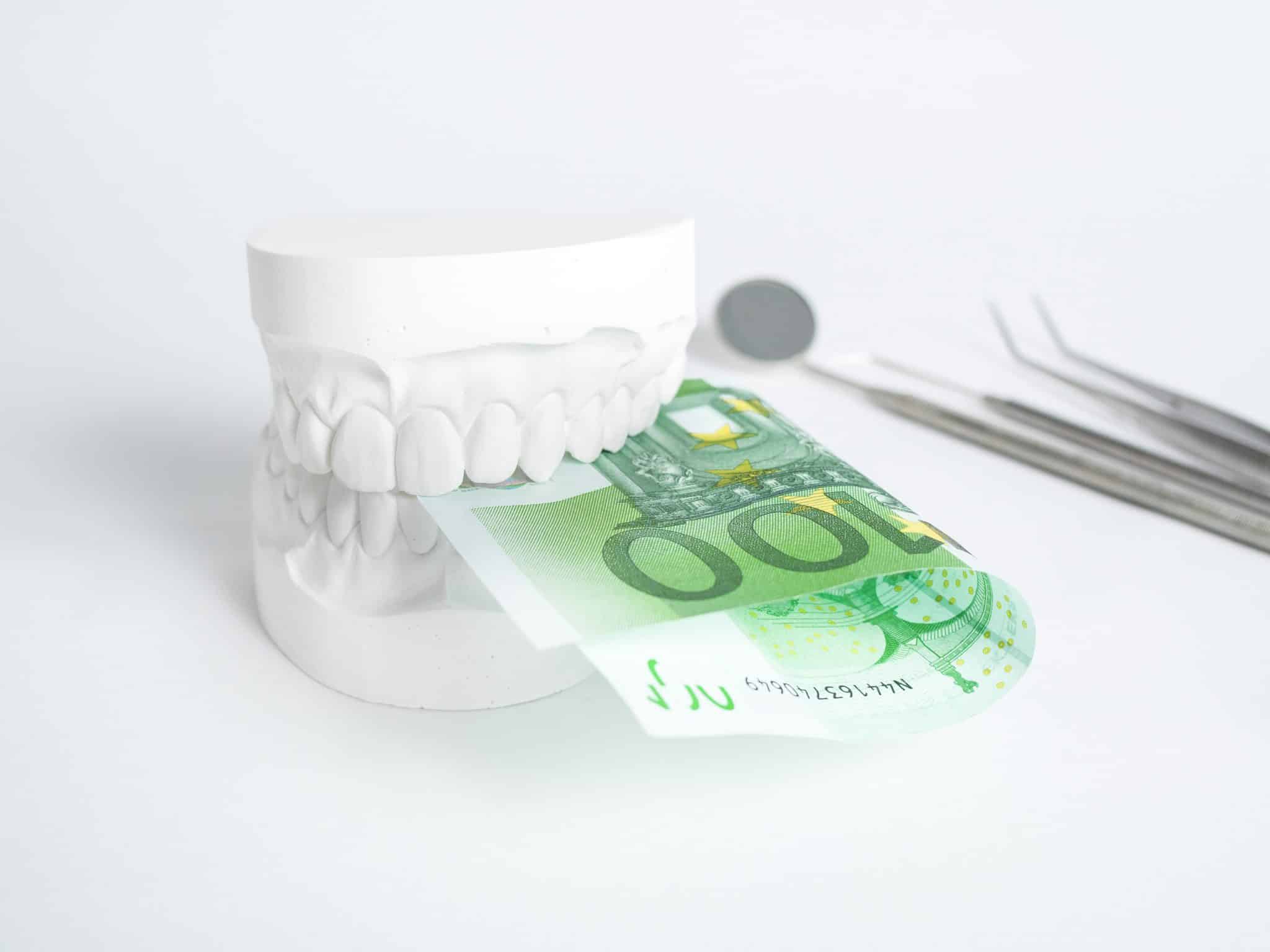 Zahnabdruck, in dem ein Hundert-Euro-Schein steckt. Im Hintergrund zahnmedizinische Instrumente.