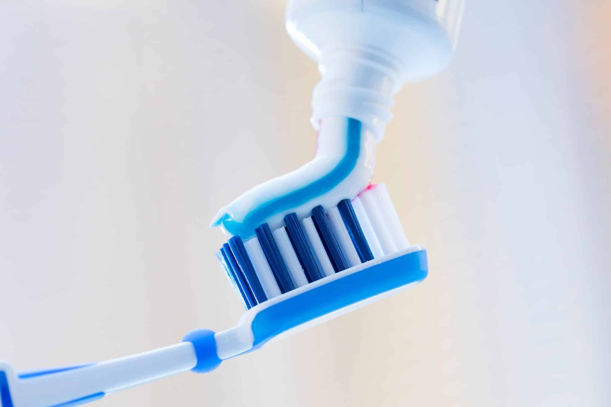 Auf blaurötlichem Hintergrund wird Zahnpasta auf eine Zahnbürste aufgetragen.