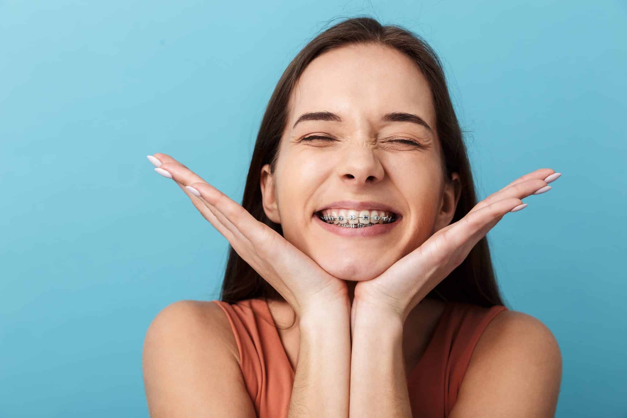 Das strahlendes Lächeln einer jungen Frau mit Zahnspange vor blauem Hintergrund.