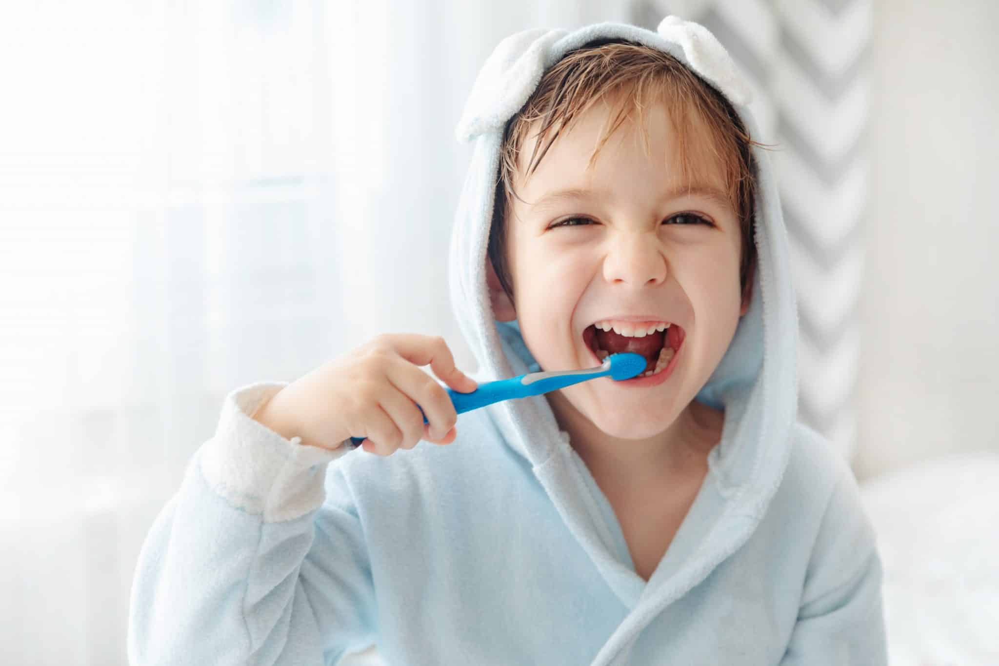 Ein lachendes Kind im Badmantel putzt sich die Zähne mit einer Zahnbürste.