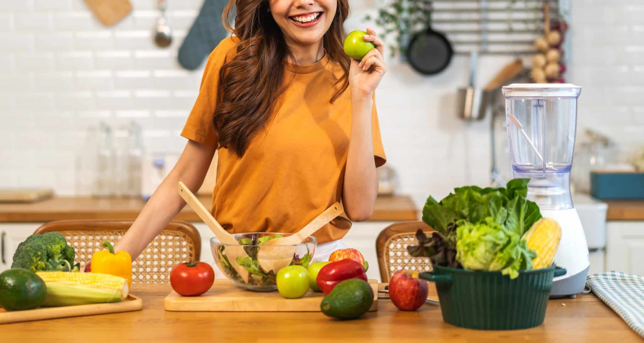 Frau in der Küche mit Gemüse und Salat auf der Arbeitsplatte.