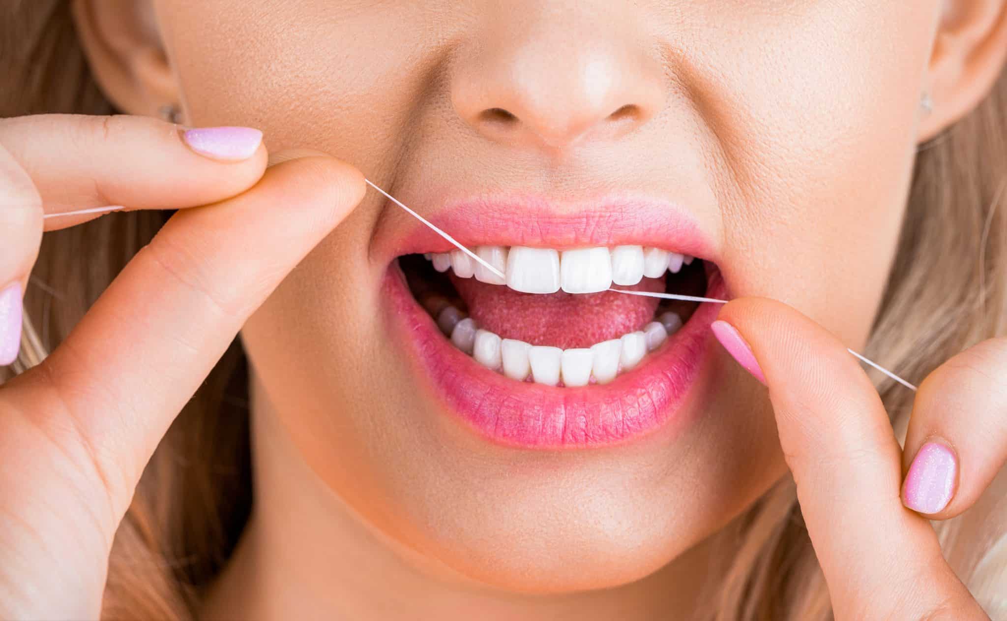 Zahngesundheit und weiße Zähne mit Zahnseide. Eine lächelnde Frau verwendet Zahnseide für Zahn- und Mundhygiene und zur Vorsorge.