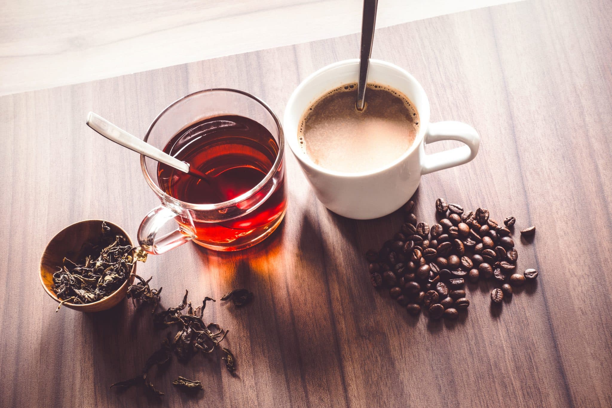 Kaffee und Tee in Tassen mit Bohnen und Teeblättern auf einer Tischplatte