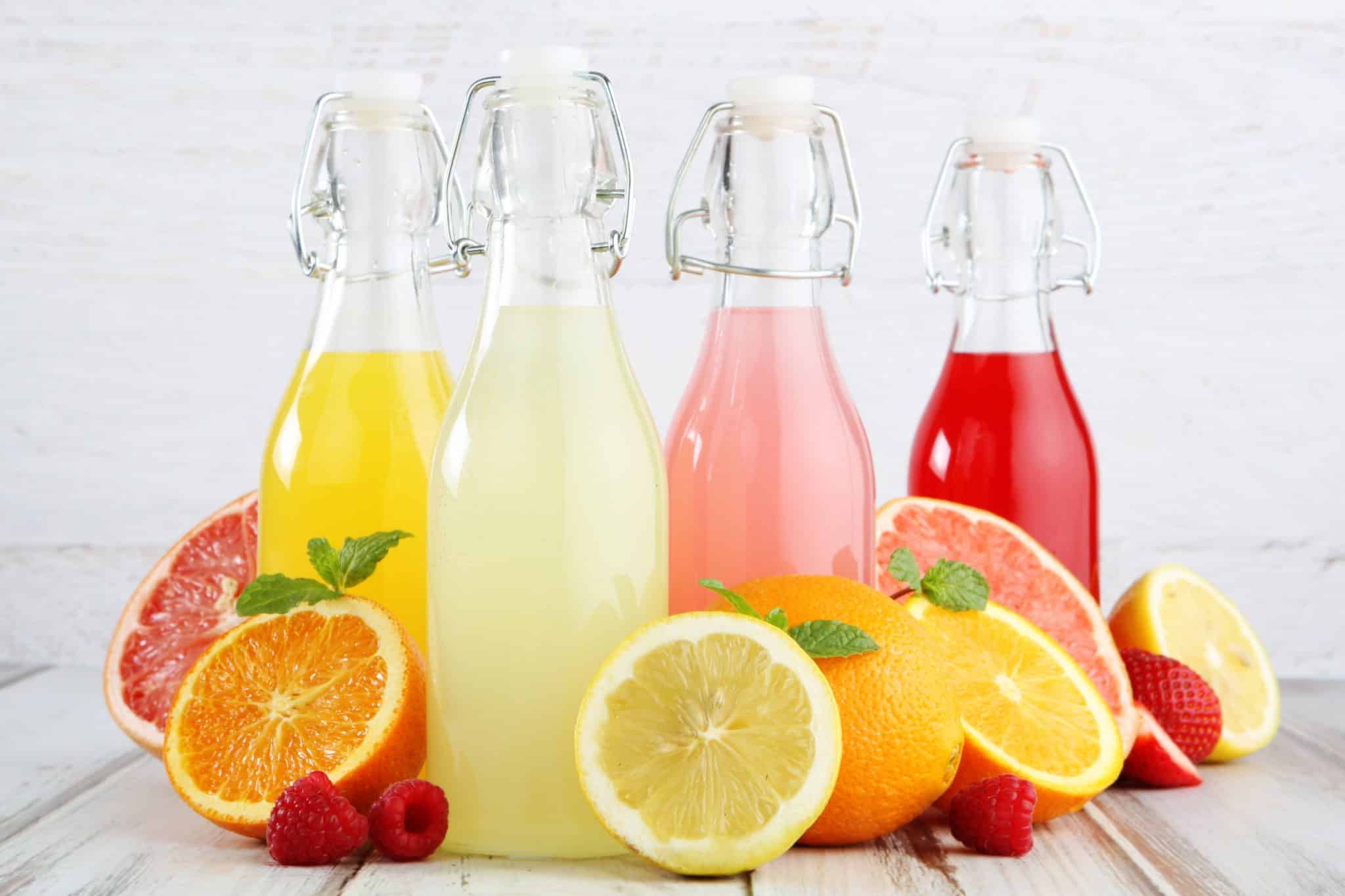 Verschiedenfarbige, säurehaltige Getränke in Flaschen und säurehaltige Früchte wie Zitrone, Orange, Grapefruit sind zu sehen.