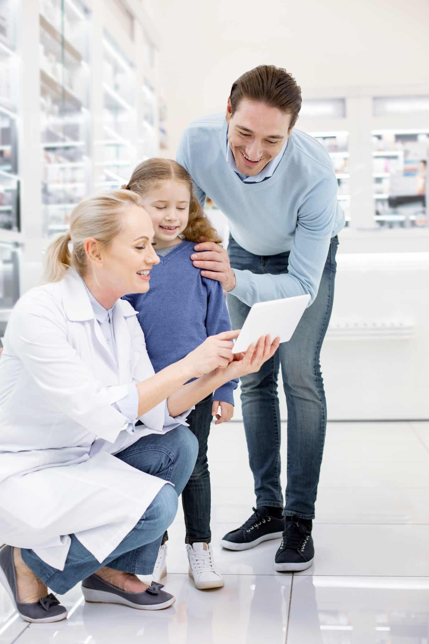 Eine Ärztin und ein Vater mit seiner kleinen Tochter sind begeistert über die innovative App einer Zahnzusatzversicherung auf einem Tablett.