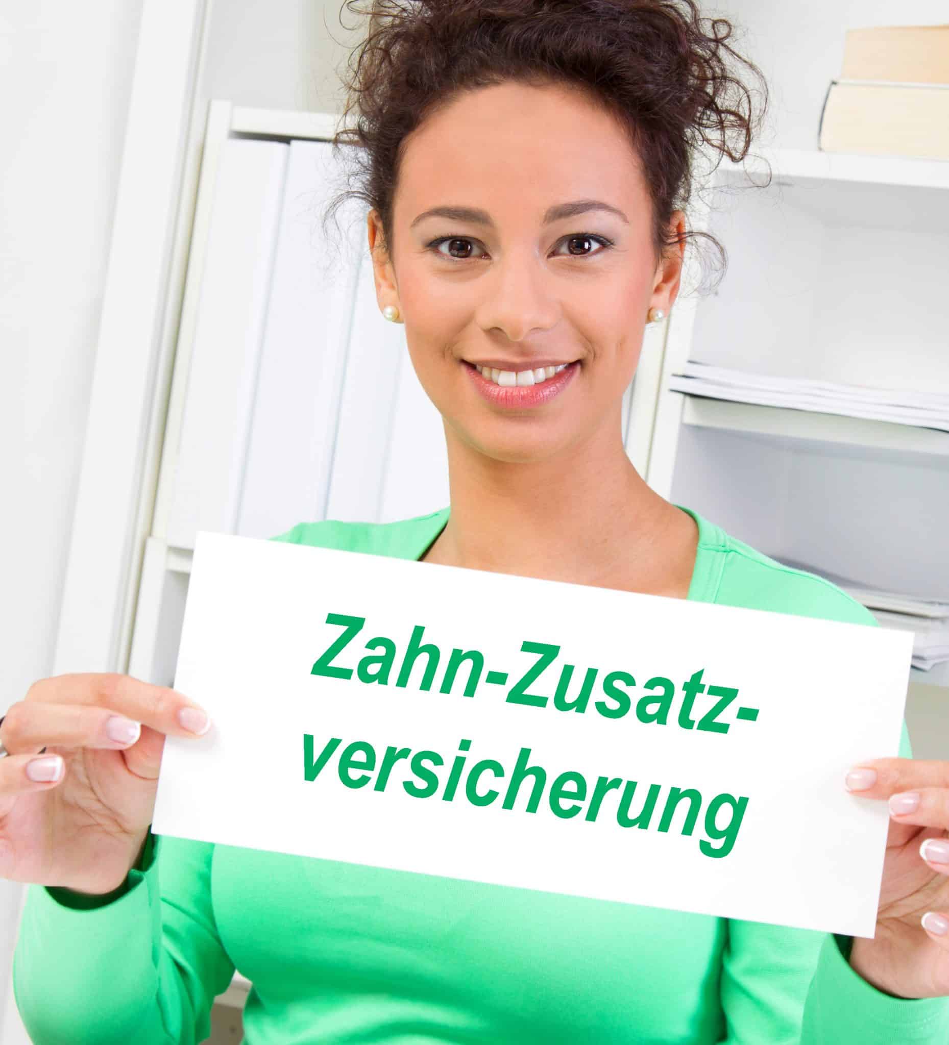 Eine junge Frau zeigt ein Schild mit dem grünem Text Zahn-Zusatzversicherung vor sich.
