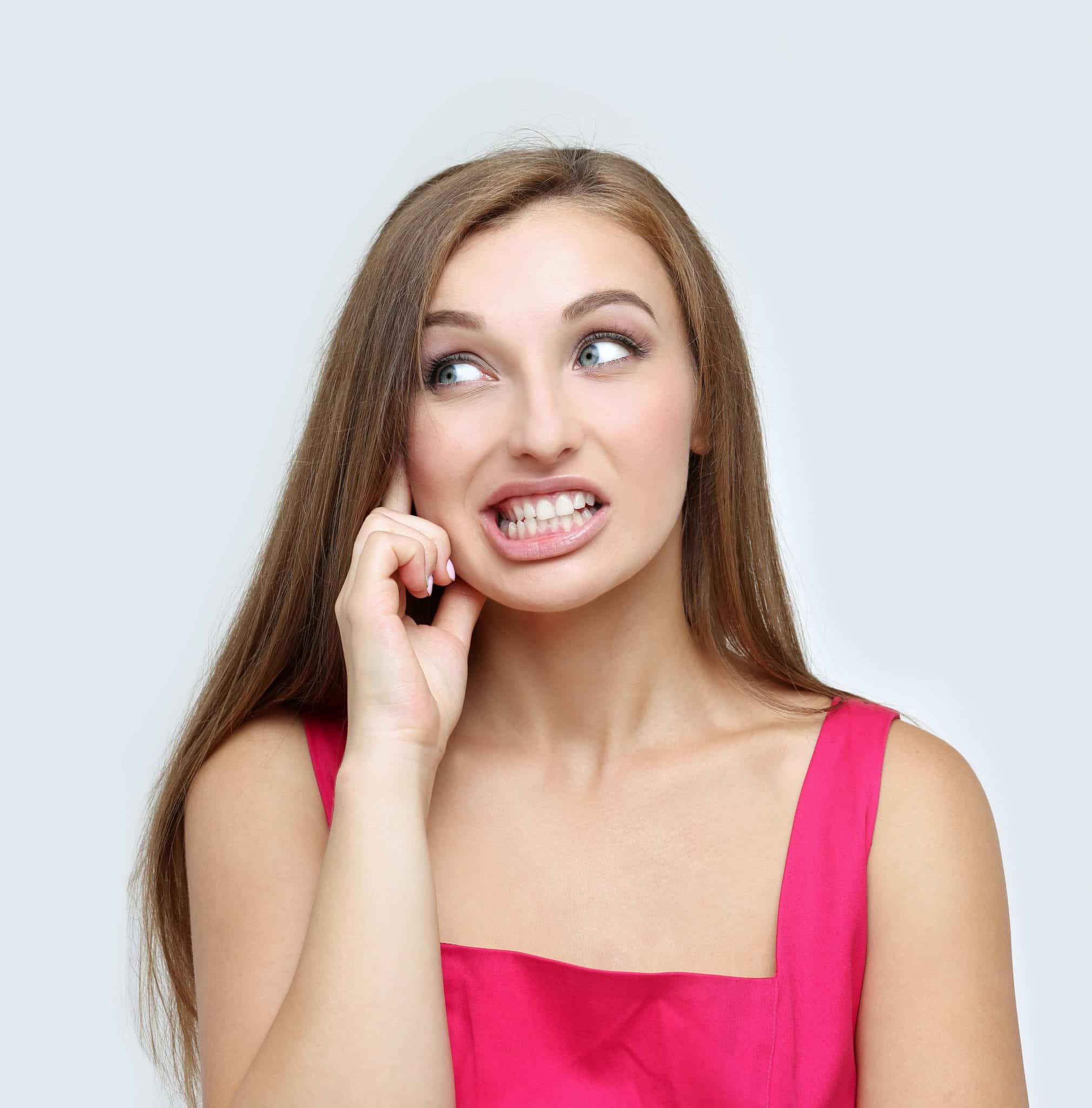 Eine junge Frau hat einen ängstlichen Gesichtsausdruck wegen ihres Problems mit dem Zähneknirschen.
