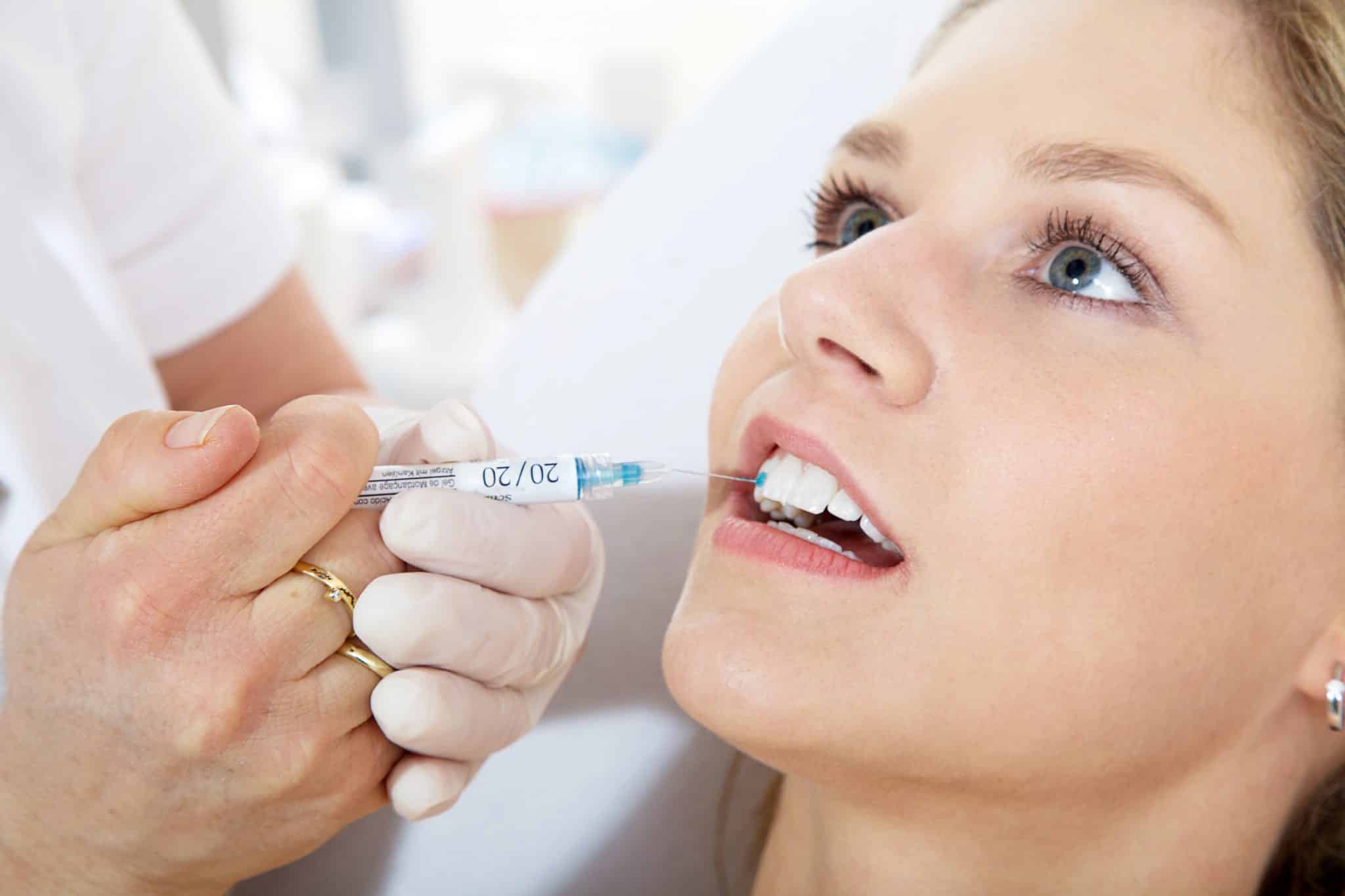 Das Foto zeigt wie ein Zahnarzt Spezialkleber bei einer jungen Frau für Zahnschmuck auf einen Zahn aufträgt.