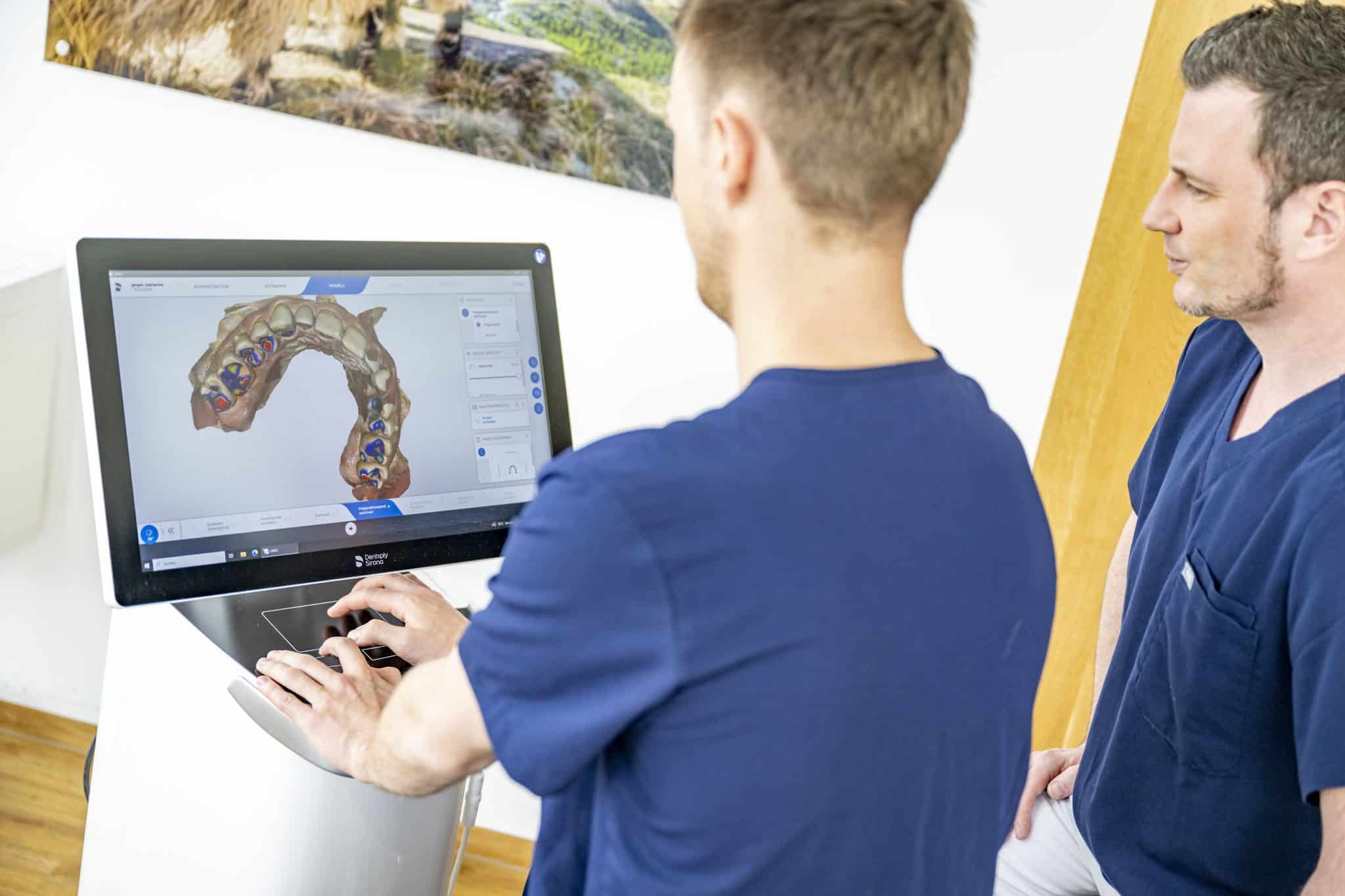 Zwei Zahnärzte der Zahnarztpraxis Dr. Geiger in Augsburg Göggingen analysieren ein digitales Zahnmodell am Monitor des CEREC-Systems.