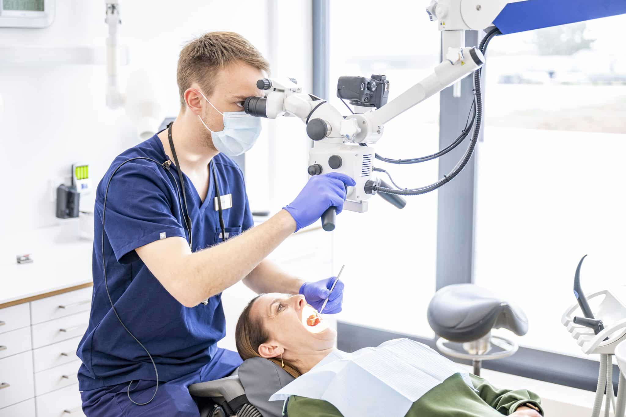 Ein Zahnarzt der Praxis Dr. Geiger Augsburg Göggingen behandelt mit Mikroskop eine Patientin.