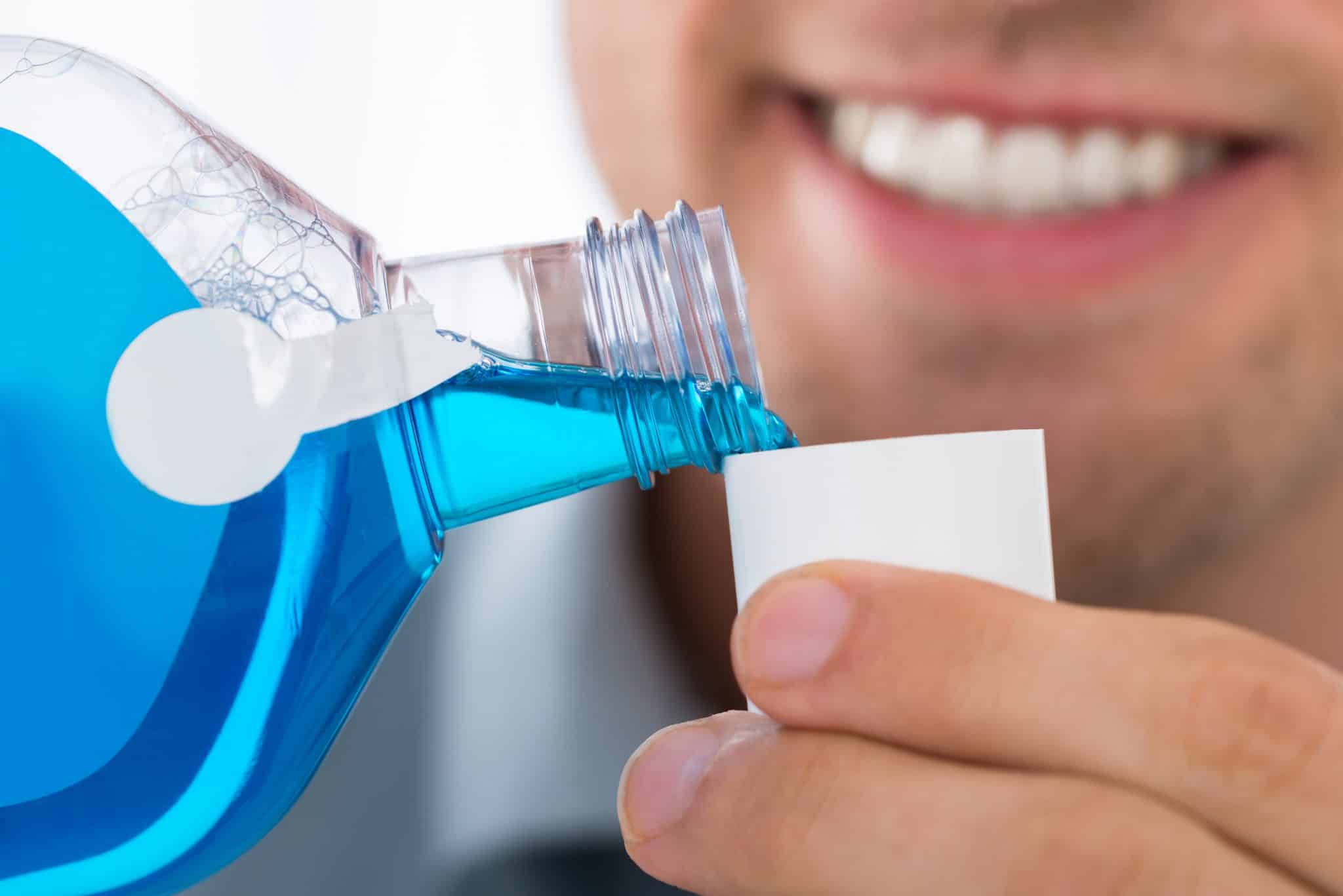 Ein junger Mann füllt ein blaues Mundspülprodukt in den Verschlussbecher der Produktflasche.