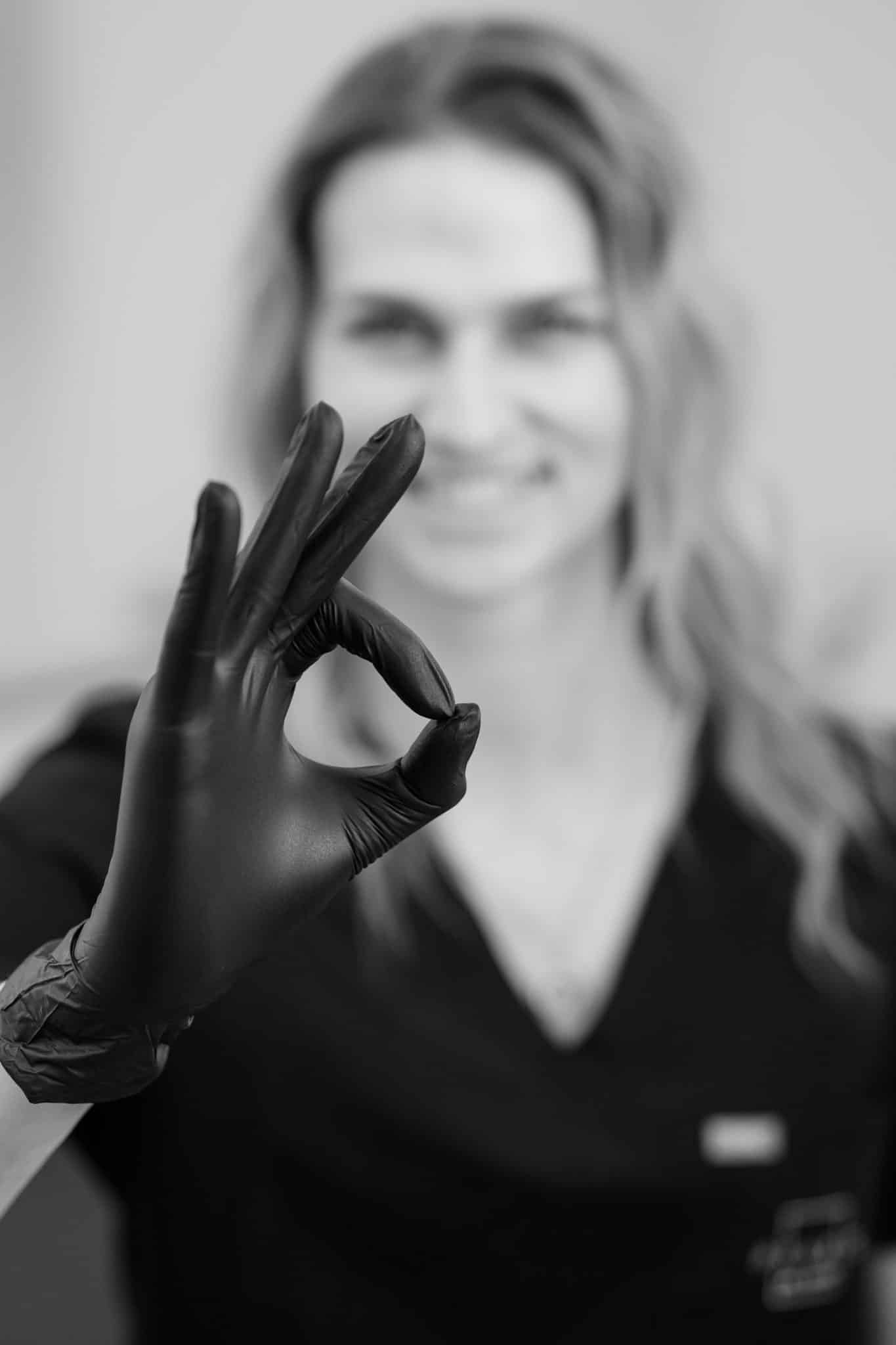 Eine junge Frau zeigt mit ihrer Geste in der Daumen und Zeigefinger einen Kreis bilden und die anderen Finger gespreizt sind, die Ausbildung zum Beruf Zahnarzt ist ausgezeichnet, vielseitig, spannend, die beste Berufswahl.